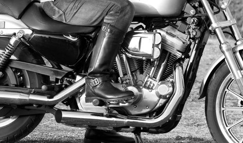 Bota alta de cuero negro apoyada en el reposapiés de una motocicleta, en una fotografía en blanco y negro.
