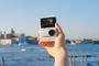 Insta360 GO 3S blanca sostenida en una mano, con la pantalla desplegada y Venecia de fondo.