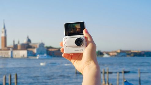 Insta360 GO 3S blanca sostenida en una mano, con la pantalla desplegada y Venecia de fondo.