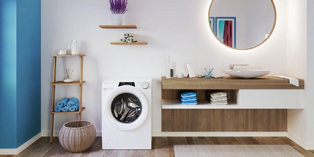 Lavadora Candy de carga frontal junto a un mueble de lavabo, con estantes y toallas.