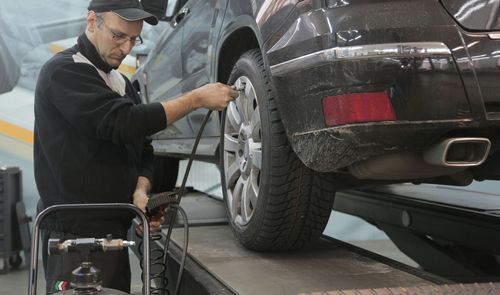Mecánico inflando el neumático de un coche con una manguera conectada a un compresor en un taller.