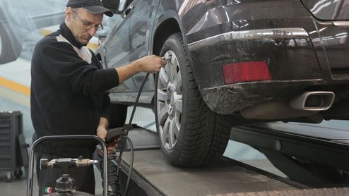Mecánico inflando el neumático de un coche con una manguera conectada a un compresor en un taller.