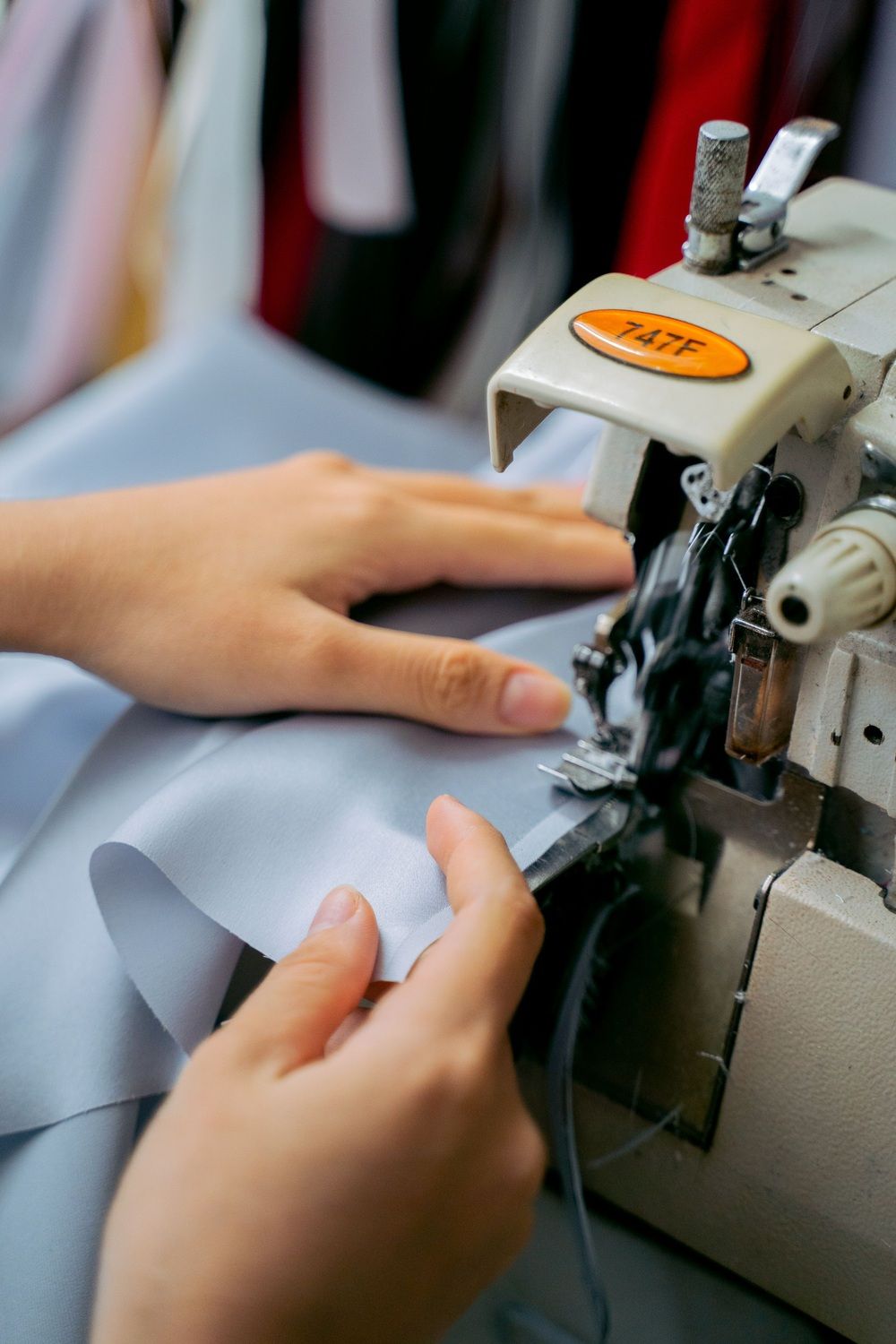 Primer plano de unas manos guiando una tela azul clara bajo la aguja de una máquina de coser.
