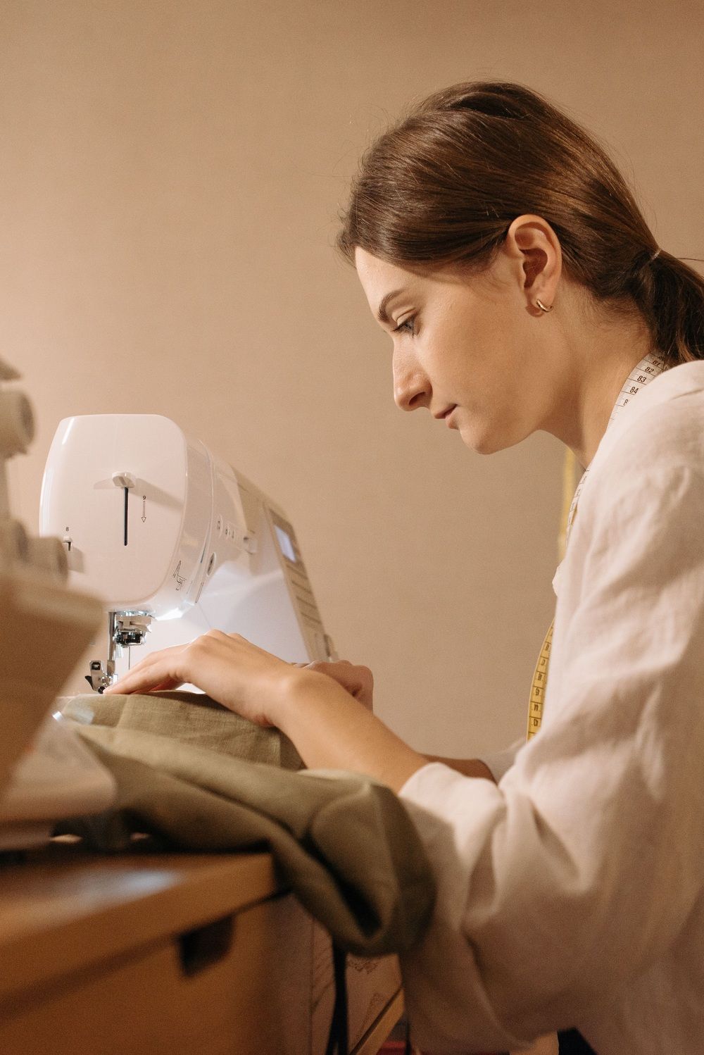 Mujer con una cinta métrica al cuello utilizando una máquina de coser blanca.