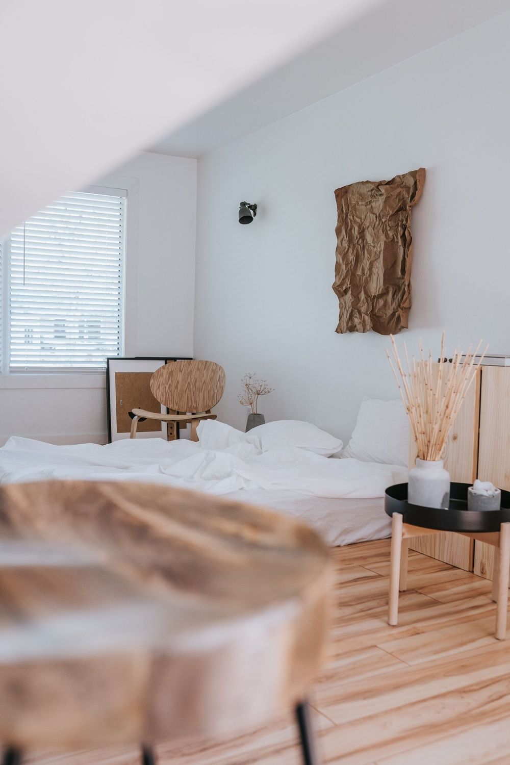 Dormitorio luminoso con un colchón bajo, ropa de cama blanca y suelo de madera.