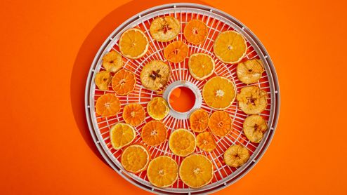 Rodajas de cítricos y manzana deshidratados en una bandeja circular sobre fondo naranja.