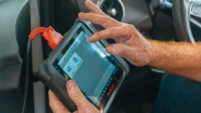 Una persona utiliza una tablet de diagnosis conectada por cable dentro de un coche.