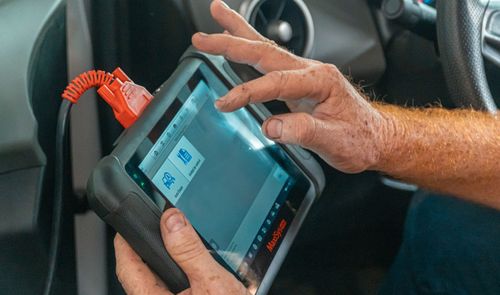 Una persona utiliza una tablet de diagnosis conectada por cable dentro de un coche.