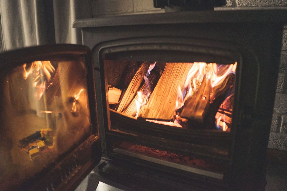 Primer plano de una estufa de leña con la puerta abierta y troncos ardiendo en su interior.