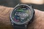 Garmin Fēnix E en una muñeca, con datos de desnivel y ritmo en pantalla y un fondo exterior desenfocado.