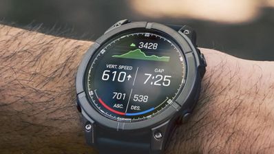 Garmin Fēnix E en una muñeca, con datos de desnivel y ritmo en pantalla y un fondo exterior desenfocado.