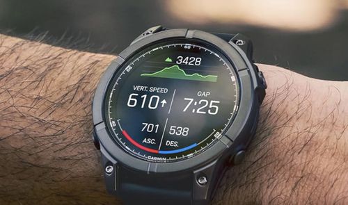 Garmin Fēnix E en una muñeca, con datos de desnivel y ritmo en pantalla y un fondo exterior desenfocado.
