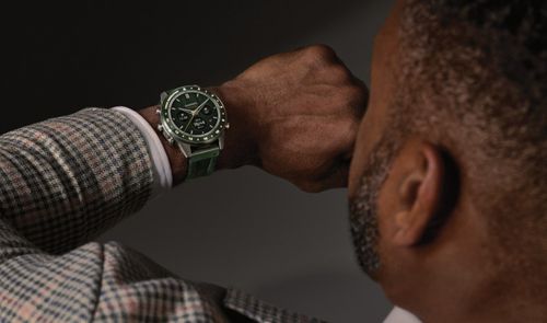 Hombre con chaqueta de cuadros consultando un reloj Garmin MARQ con esfera y correa verdes.