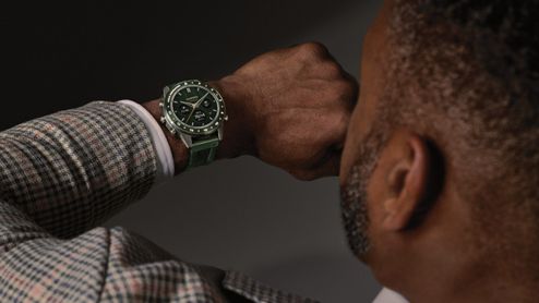 Hombre con chaqueta de cuadros consultando un reloj Garmin MARQ con esfera y correa verdes.
