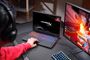 Una persona utiliza un portátil HyperX OMEN 15 con teclado iluminado junto a un monitor gaming en un escritorio.