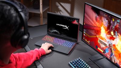 Una persona utiliza un portátil HyperX OMEN 15 con teclado iluminado junto a un monitor gaming en un escritorio.