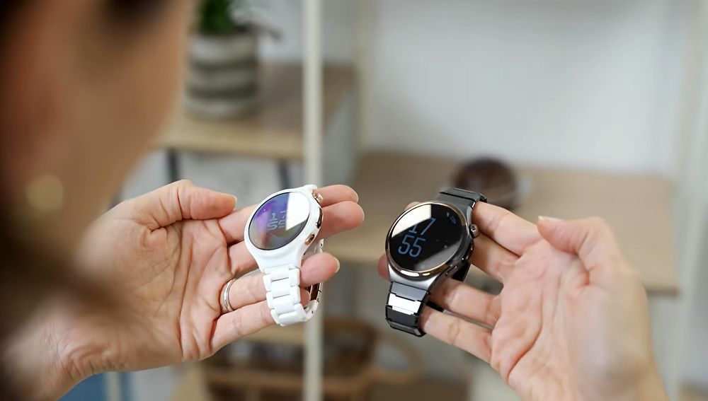 Dos relojes Huawei con correas de eslabones blanca y oscura sostenidos en las manos.
