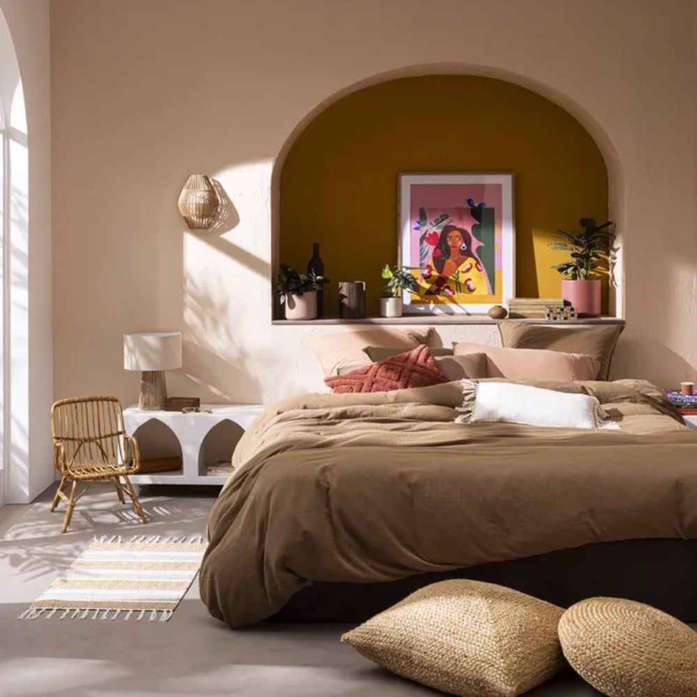 Dormitorio en tonos tierra con ropa de cama marrón, cojines y un arco decorativo de color ocre.