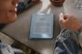 Persona junto a un Kindle azul sobre una mesa mientras toma un café.