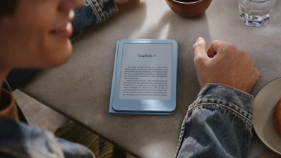 Persona junto a un Kindle azul sobre una mesa mientras toma un café.