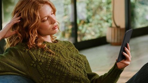 Mujer leyendo un Kindle mientras descansa en un sillón en casa.