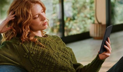 Mujer leyendo un Kindle mientras descansa en un sillón en casa.
