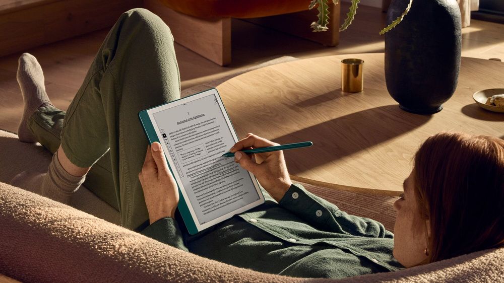 Una persona utiliza el lápiz de un Kindle Scribe mientras descansa en un sofá.
