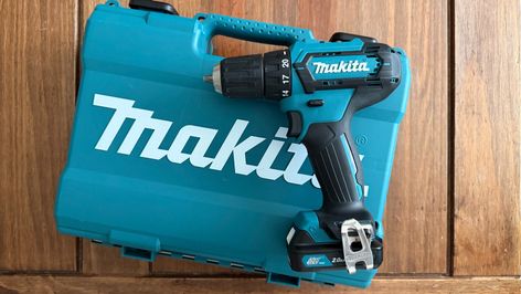 Taladro inalámbrico Makita apoyado sobre su maletín de transporte azul en una superficie de madera.