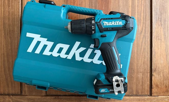 Taladro inalámbrico Makita apoyado sobre su maletín de transporte azul en una superficie de madera.
