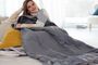 Mujer descansando en un sofá, arropada con una manta eléctrica gris.