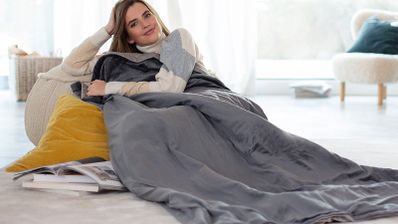 Mujer descansando en un sofá, arropada con una manta eléctrica gris.