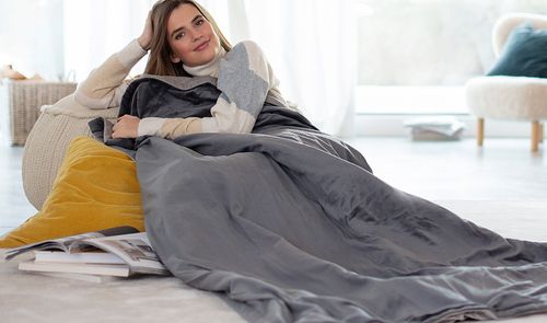 Mujer descansando en un sofá, arropada con una manta eléctrica gris.