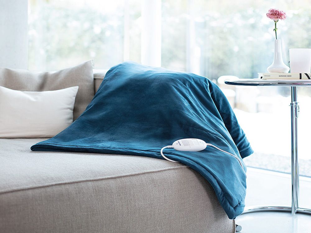 Manta eléctrica azul extendida sobre un sofá gris, con el mando blanco sobre el tejido.