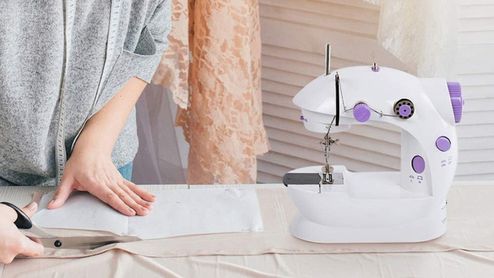Mujer preparando una tela sobre una mesa junto a una máquina de coser portátil blanca con controles violetas.