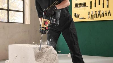 Primer plano de un martillo perforador Parkside negro y dorado, utilizado con un cincel para romper un bloque de obra.