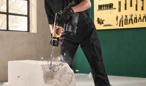 Primer plano de un martillo perforador Parkside negro y dorado, utilizado con un cincel para romper un bloque de obra.