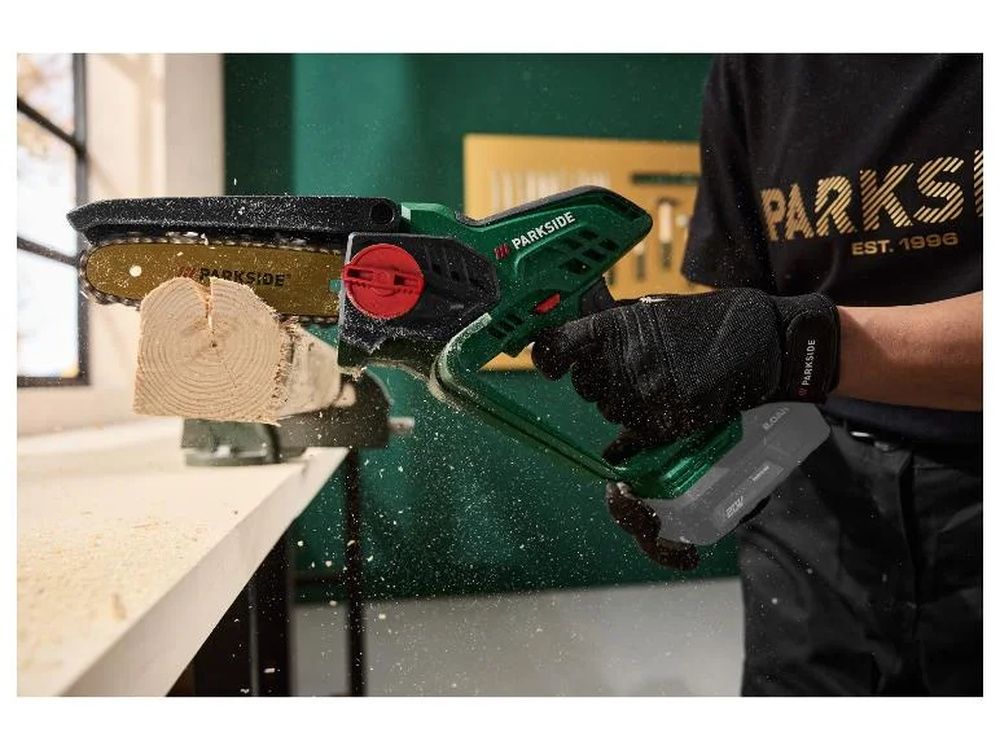Primer plano de una minisierra Parkside cortando una pieza de madera sujeta a un banco de trabajo, con serrín en el aire.