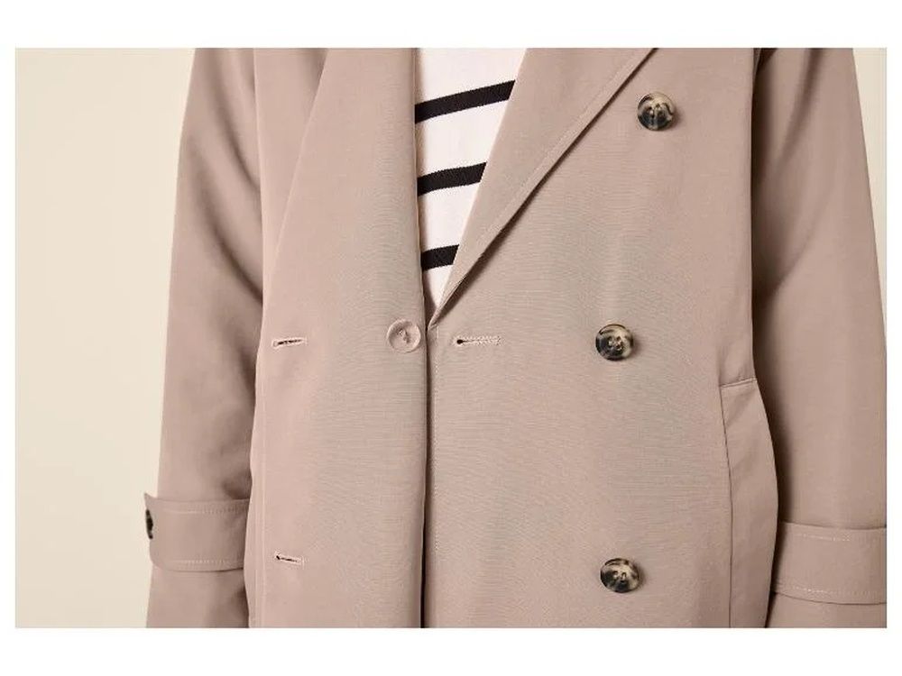 Detalle de una gabardina beige de doble botonadura sobre una camiseta de rayas