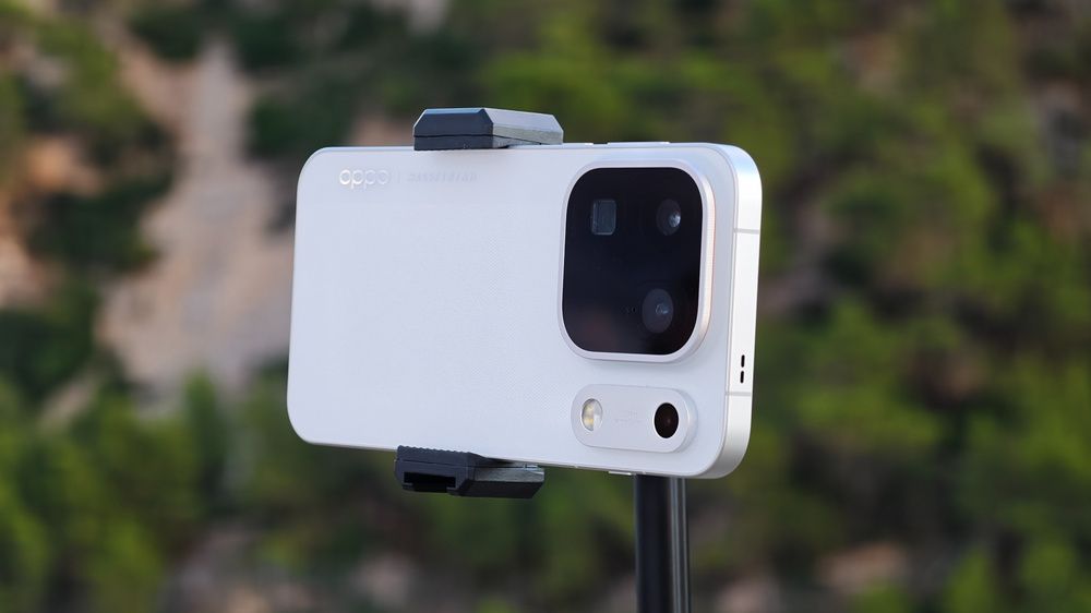 Móvil OPPO blanco sujeto en horizontal, con sus cámaras traseras visibles y vegetación de fondo.