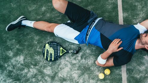 Jugador de pádel descansando sobre la pista junto a su pala y varias pelotas.
