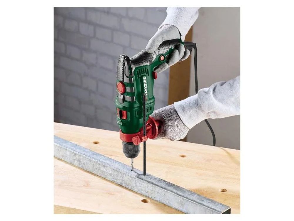 Persona con guantes utilizando un taladro Parkside sobre un perfil metálico apoyado en un banco de madera.