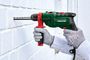 Taladro de impacto Parkside verde y rojo perforando una pared de ladrillo blanco, sujetado con guantes de trabajo.