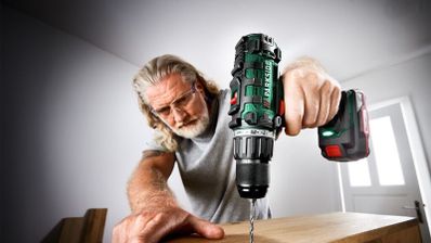Hombre con gafas de protección utilizando un taladro inalámbrico Parkside para perforar un tablón de madera.