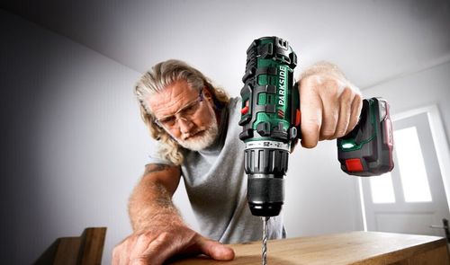 Hombre con gafas de protección utilizando un taladro inalámbrico Parkside para perforar un tablón de madera.