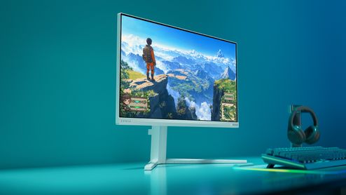 Monitor Philips Evnia 24M2N3201P blanco sobre un escritorio con iluminación azul, junto a un teclado y unos auriculares.