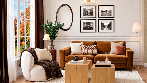 Salón con sofá marrón, sillón blanco con manta, mesas de madera y cojines en tonos beige y teja.
