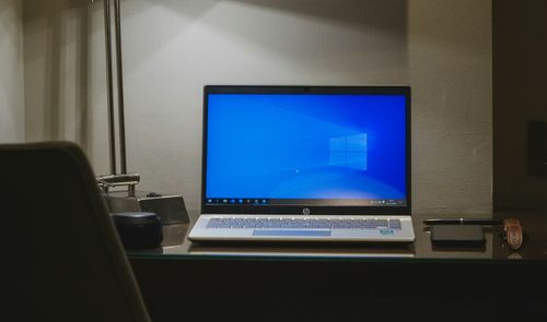 Portátil HP abierto sobre un escritorio, con Windows en pantalla y una lámpara a su lado.