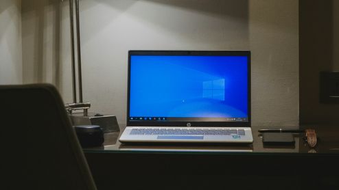 Portátil HP abierto sobre un escritorio, con Windows en pantalla y una lámpara a su lado.