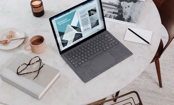Ordenador portátil sobre una mesa junto a una taza de café, un cuaderno y material de trabajo.