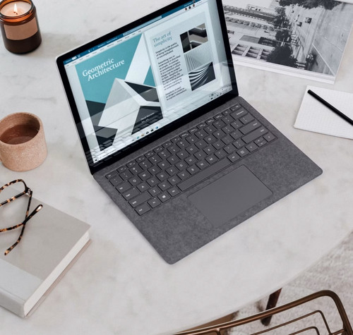 Ordenador portátil sobre una mesa junto a una taza de café, un cuaderno y material de trabajo.